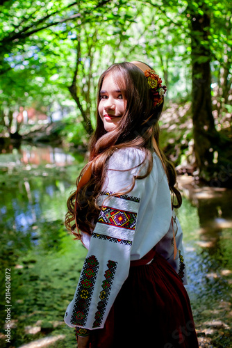 Young Ukrainian woman in a traditional embroidered costume standing in a green forest, combining cultural heritage, femininity and a close connection with nature.