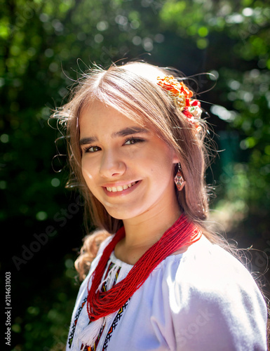 Portrait of a young Ukrainian woman in traditional embroidered clothing and folk accessories in a green forest, representing culture, heritage and national identity.