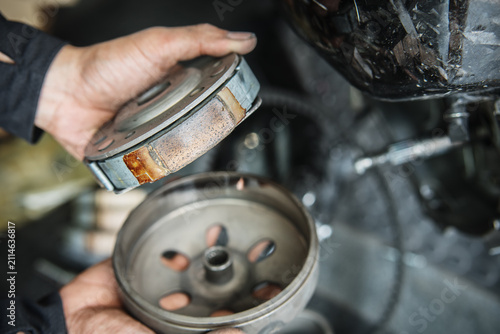 Mechanic inspecting glazed and worn scooter clutch shoes showing surface wear and friction loss