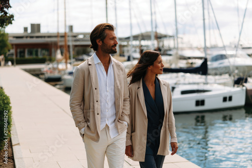 A charming couple dressed in contemporary attire enjoys a leisurely stroll by the waterfront, creating a perfect blend of style, romance, and lifestyle.