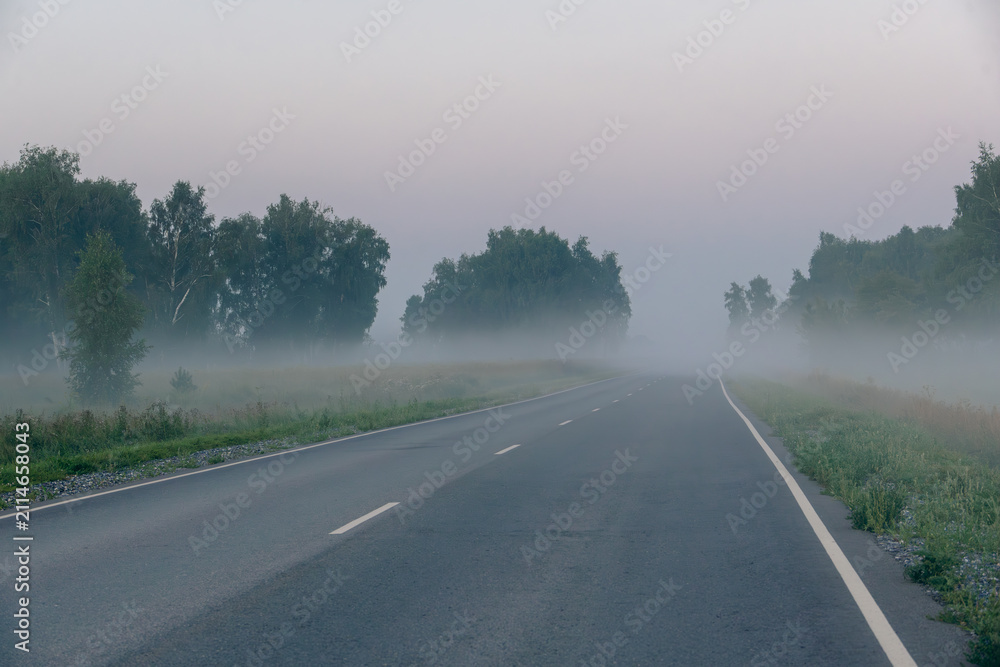 Obraz premium Car headlights glowing through thick morning fog on empty asphalt road