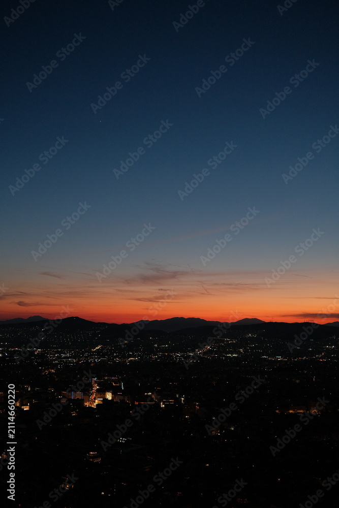 Fototapeta premium Fiery sunset horizon viewed from Mount Lycabettus in Athens, Greece, with the city below silhouetted beneath a glowing orange and blue twilight sky.