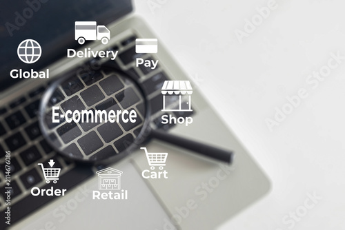 E-commerce and online shopping concept. Magnifying glass on a laptop keyboard focusing on E-commerce text with retail, delivery, and payment icons. Digital marketing and global business.