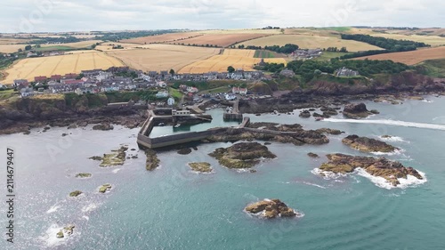 Aerial drone tracking shot over the historic fishing village and harbour of St Abbs, moving in a semi-circular motion to showcase the rugged Berwickshire coast, rocky bay, and North Sea in Scotland.