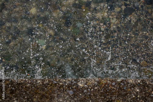 Obraz na plátne Clear water splashes over dark stones along a rocky edge