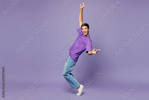 Full body young man wear violet t-shirt casual clothes standing on toes dancing lean back have fun spreading hands isolated on plain pastel light purple background studio portrait. Lifestyle concept.