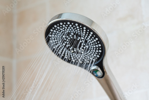 A close-up view of a handheld showerhead spraying a steady stream of water, designed for bathroom use.