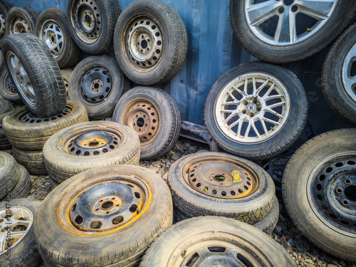 Pile of Used Car Tires and Wheels Against Metal Wall