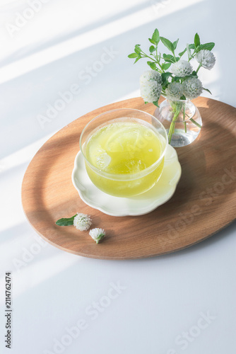 Cold green tea with ice in a glass on a wooden tray with white flowers
