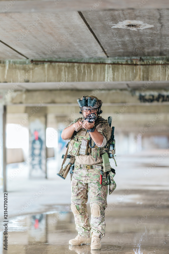 Naklejka premium Military tactical operator holds rifle while clearing abandoned concrete building interior