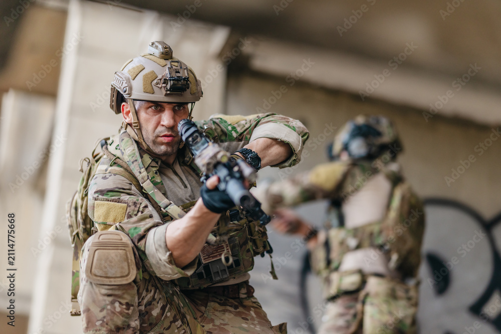 Fototapeta premium Military tactical operator holds rifle while clearing abandoned concrete building interior