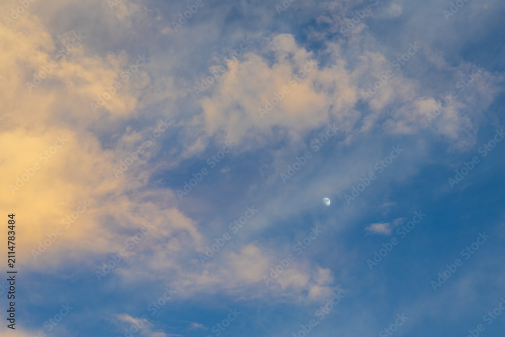 Fototapeta premium Golden cloud and blue sky with partial moon visible at dusk, soft warm light and airy texture creating calm atmospheric scene