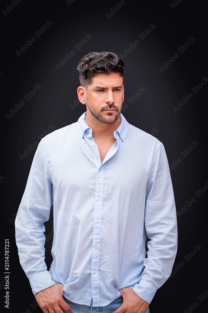 Fototapeta premium Handsome young man in a light blue button-down shirt portrait against isolated black background