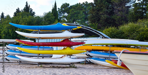 Obraz na plátně Colorful kayaks stacked on a rack at a beach, surrounded by greenery and a clear