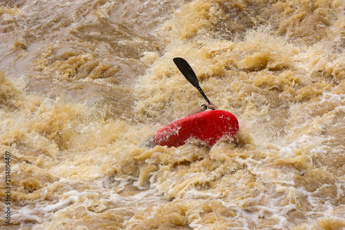 Foto Red kayak capsized in turbulent muddy whitewater rapids showing paddle amid frot