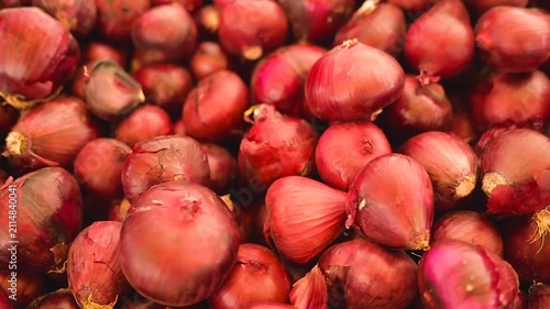 Red onion bulbs pile displayed fresh at market counter. UHD slow motion footage