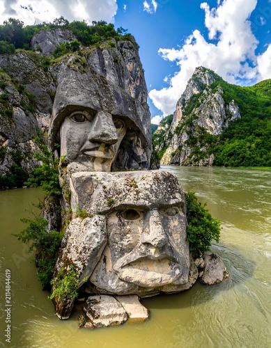 A river flows between two rocky cliffs with carved stone faces