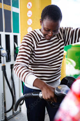 Foto Woman filling up car with fuel at a gas station, smiling subtly