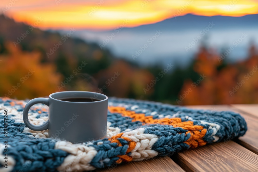 Fototapeta premium Coffee mug on a cozy knitted blanket with autumn mountain sunrise warmth view