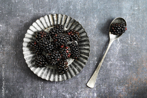 Fresh organic blackberries in a small metal plate and a spoon on dark rustic background