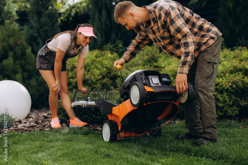 Foto Couple inspecting engine of lawn mower for repair