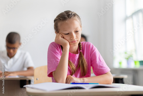 Cuadro en lienzo Tired schoolgirl resting her head on one hand beside an open notebook during cla