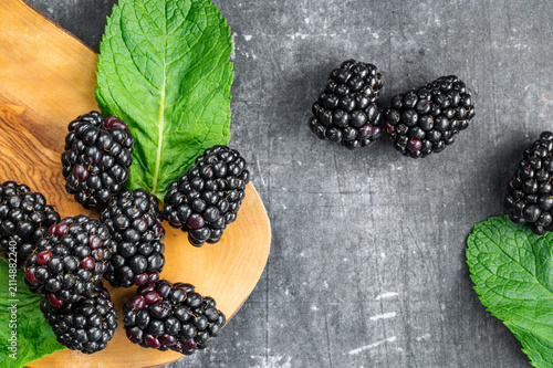 Fresh blackberries with mint leaves on a wooden board and dark background