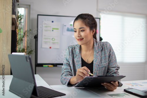 Asian businesswoman working with tablet and taking notes in modern office.