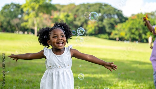 Joyful young African American girl with curly hair chasing iridescent bubbles in a sunny park