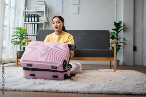 Young woman packing pink suitcase for travel trip at home.