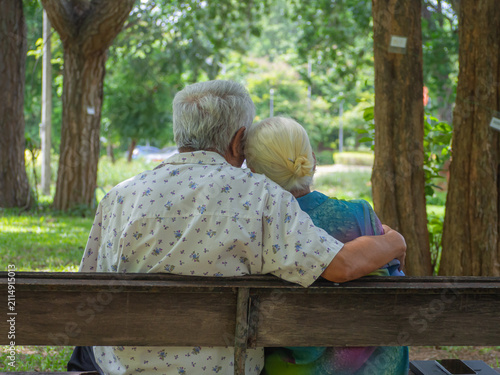Fotografie A happy senior woman resting her head gently on her partner's shoulder while sitting outdoors on a wooden park bench, expressing trust, comfort, and lifelong romance