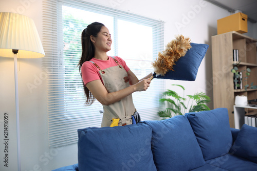 Obraz na plátně Woman feeling displeased with dust and dirt, trying to clean her living room using a feather duster and cushion