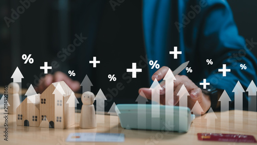 Financial advisor calculates mortgage interest rate increase utilizing calculator near wooden houses credit cards digital overlay graphics representing inflation growth.