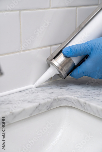Hand applying caulk to marble countertop with blue gloves  