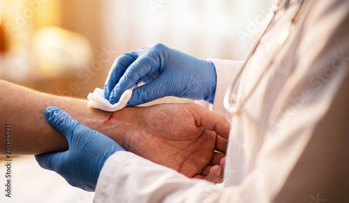 Healthcare professional cleans a small superficial cut on the wrist using sterile gauze during wound treatment in a modern medical clinic. Close-up first aid and professional healthcare concept.