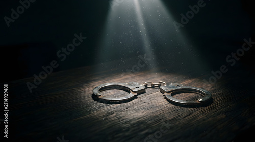 Metal handcuffs on a wooden table. Steel shackles representing crime and law enforcement.