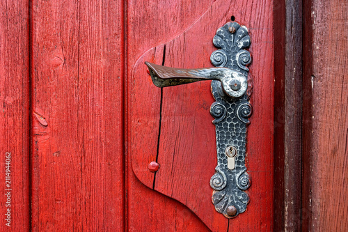 Ornamental forged steel door handle and lock plate installed on a painted red vertical timber door. Copy space