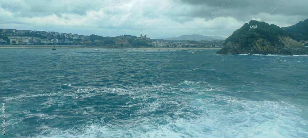 Fototapeta premium Vista panorámica de la bahía y la costa marítima bajo cielo nublado en San Sebastián, España.