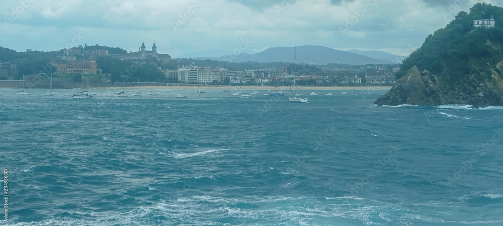 Fototapeta premium Vista panorámica de la bahía y la costa marítima bajo cielo nublado en San Sebastián, España.