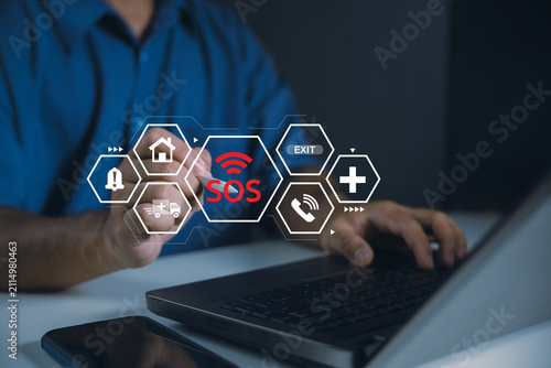 Business professional using a laptop with digital SOS emergency interface, ambulance, medical cross, home safety, exit alert, hotline, crisis response, and urgent assistance technology.