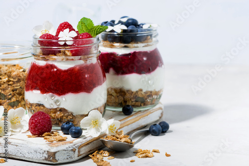 sweet desserts with granola, berry and fruit puree in jars on white wooden board