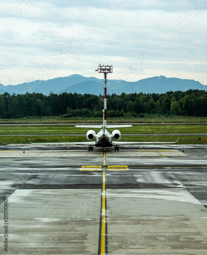 Rear view of a private aircraft aligned on a rain soaked airport apron with dramatic mountain backdrop and expansive cloudy sky creating balanced aviation composition with copy space