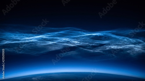Stunning view of noctilucent clouds glowing brightly above the curved horizon of earth in the deep blue mesosphere during the twilight hours of a quiet night in outer space