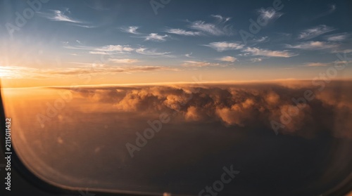 Aerial view through airplane window of golden sunset clouds and expansive ocean horizon during high altitude flight at dusk offering a peaceful perspective of the sky with captures breathtaking aerial