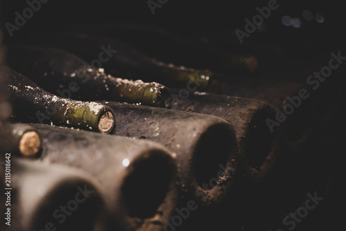 A close-up of dusty wine bottles stored horizontally in a dark cellar, evoking age, tradition, and the passage of time.
