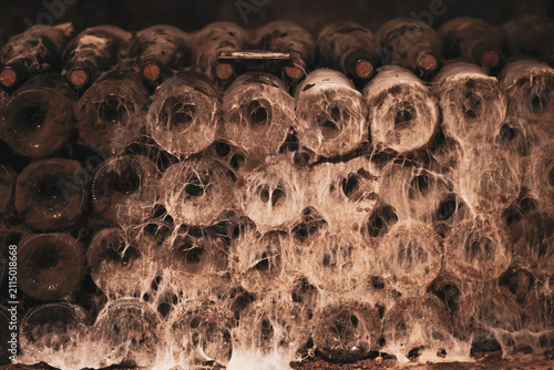A stack of old wine bottles covered in thick cobwebs and dust inside a cellar, illustrating decades of undisturbed aging.