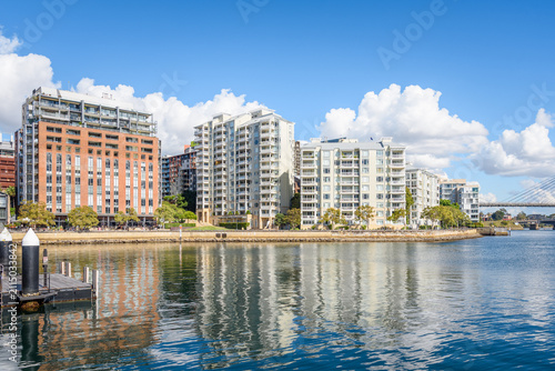 Modern apartment blocks in a waterfront development on a sunny autumn day.  A floating wooden jetty is in foreground. 