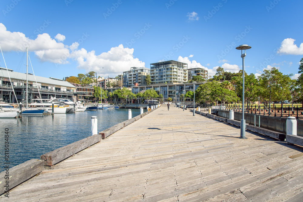 Naklejka premium Modern apartment buildings in a waterfront development on a sunny autumn day. A wooden pier and moored boats are in foreground. 