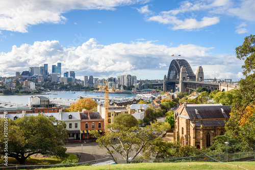 Sydeny Harbour bridge and North Sydney skyline as seen from Observatory Hill on a sunny autumn day. Old terraced house along a street  inthe historic district of the Rocks are in foreground.