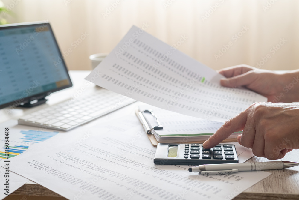 Obraz premium Hands performing essential accounting tasks, using a calculator and reviewing financial documents and data on a computer screen, signifying meticulous budgeting and reporting